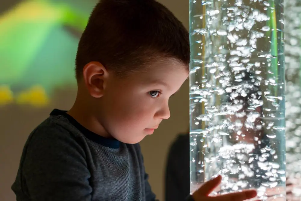 Young child boy pressing his against a lamp with bubbles inside