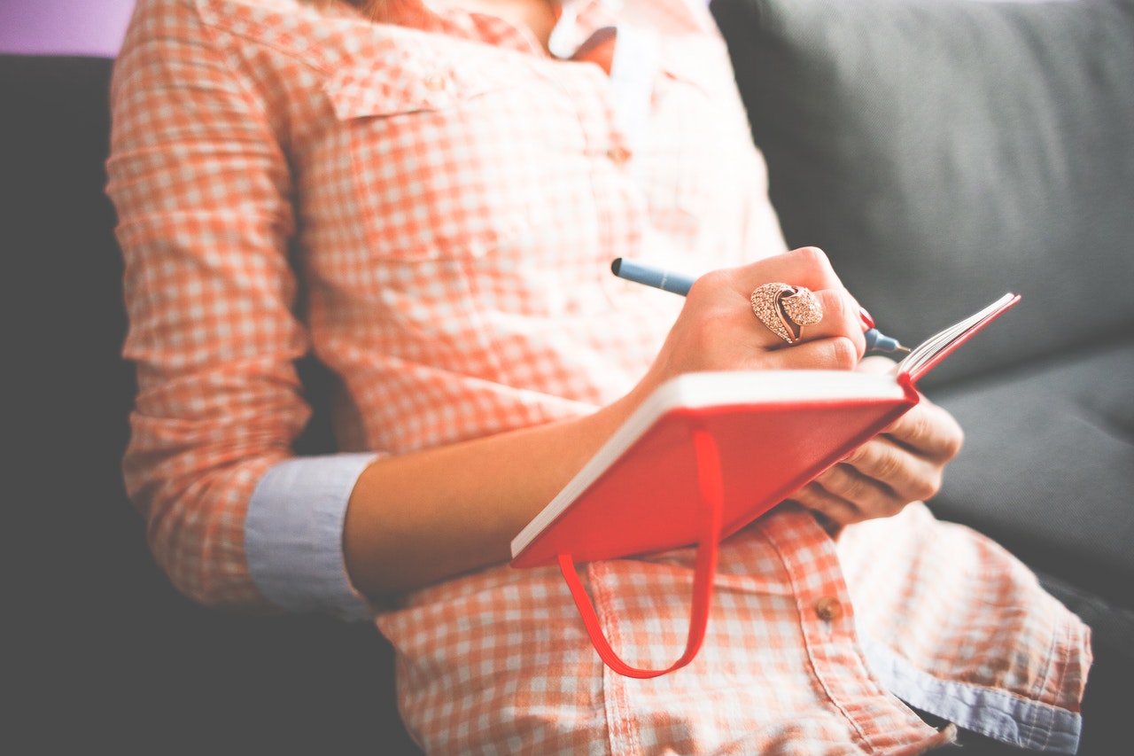 Woman in shirt writing in red journal