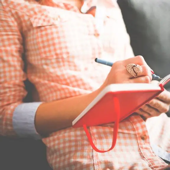 Woman in shirt writing in red journal