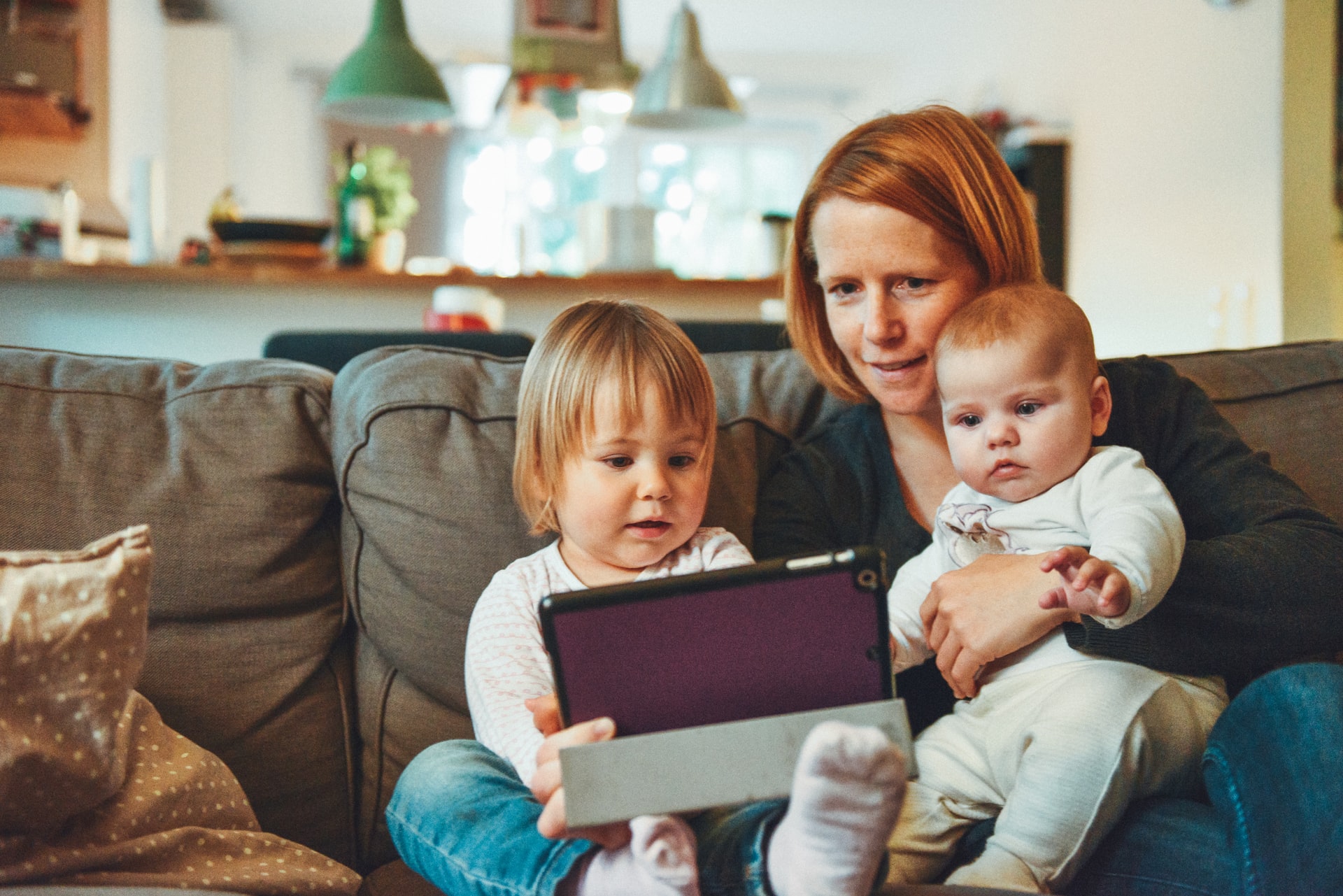 mum-with-toddler-and-baby-sitting-on-sofa-using-tablet