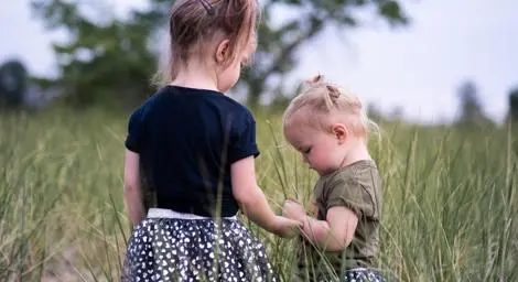 two-young-girls-standing-in-a-field-holding-hands-with-their-backs-to-the-camera