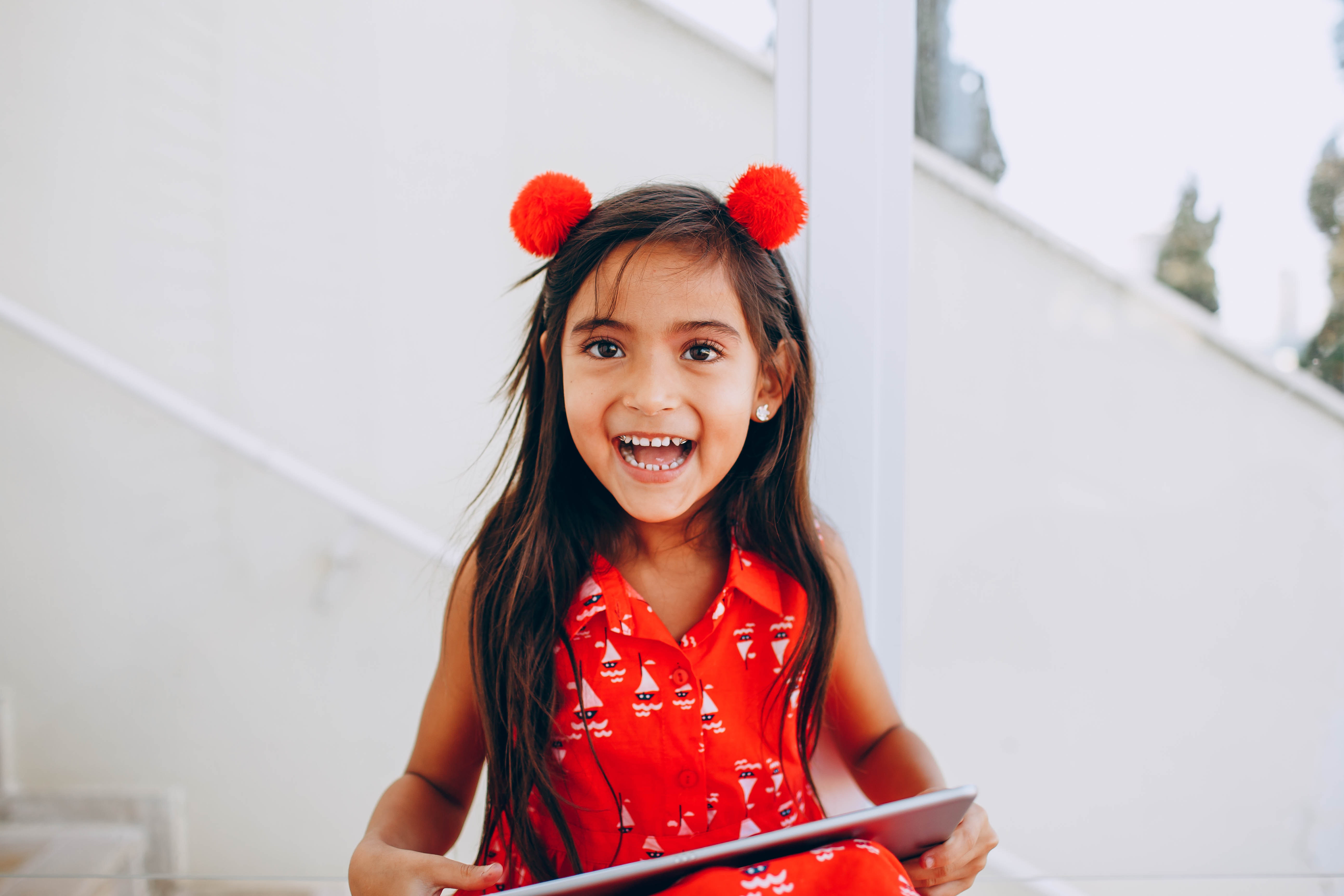 smiling-girl-wearing-red-pompon-headband-holding-tablet