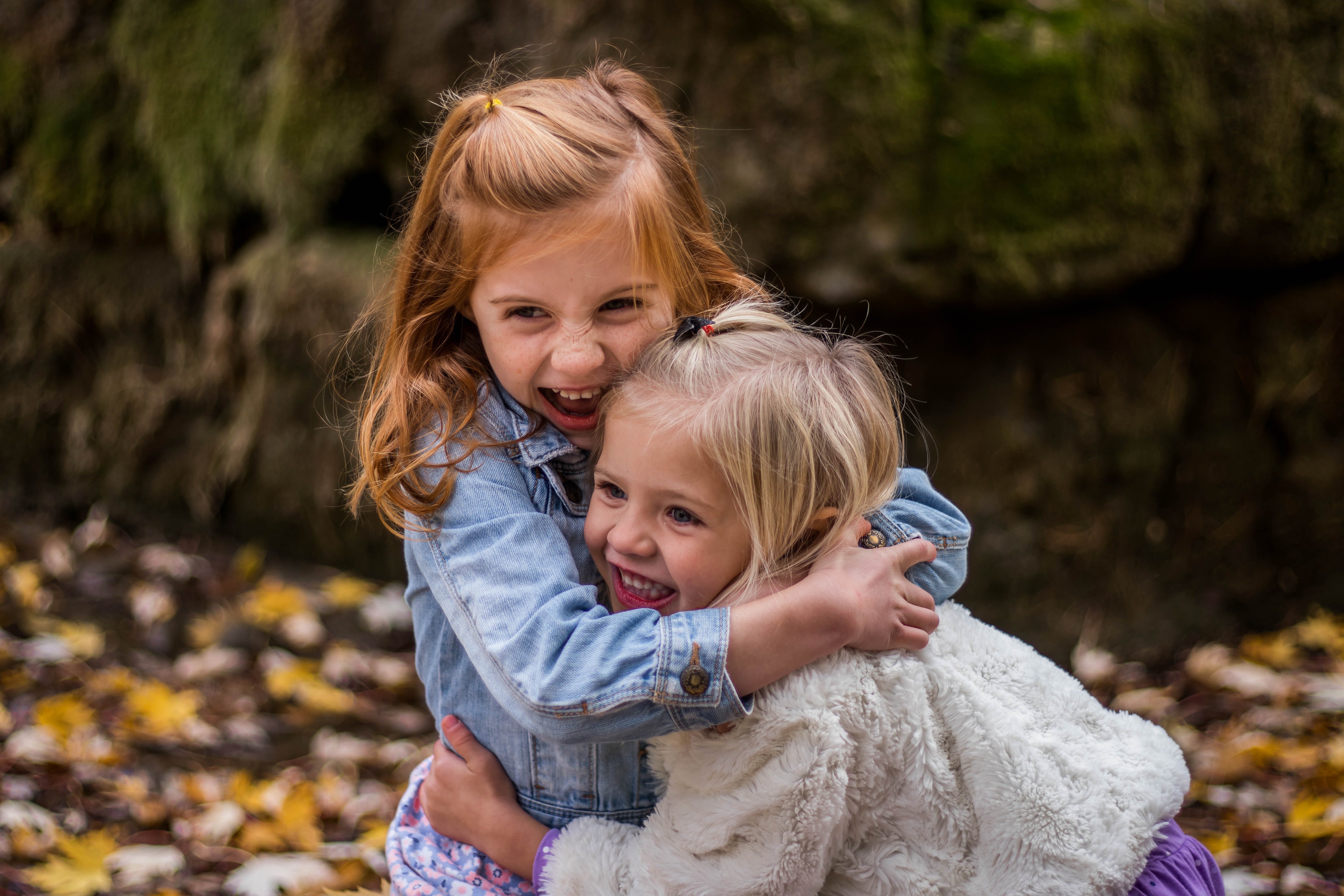Two girls hugging autumn leaves on the ground
