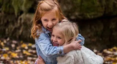 Two girls hugging autumn leaves on the ground