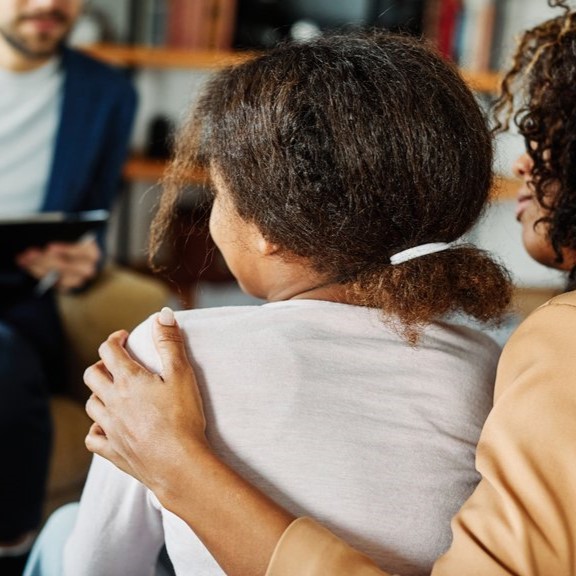 Woman holding girl's shoulder facing a social worker